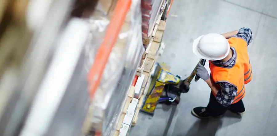 In this close up shot, a warehouse worker is using a pallet jack to move some cargo.