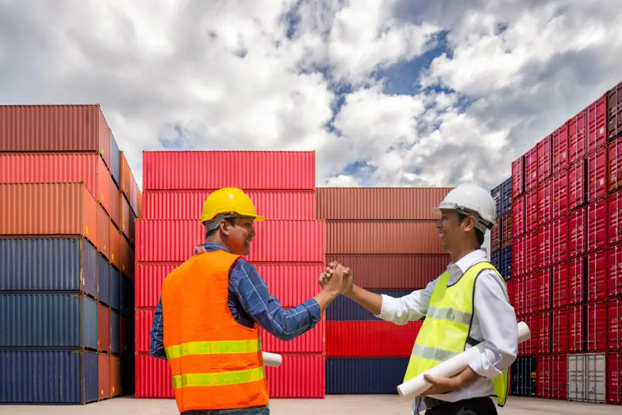 Workers in a shipping yard shaking hands and smiling